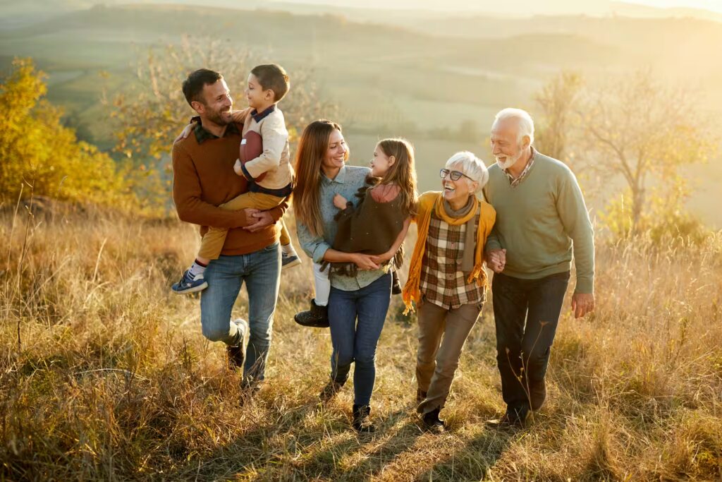 Famille multigénérationnelle marchant ensemble dans un champ au coucher du soleil souriante et complice